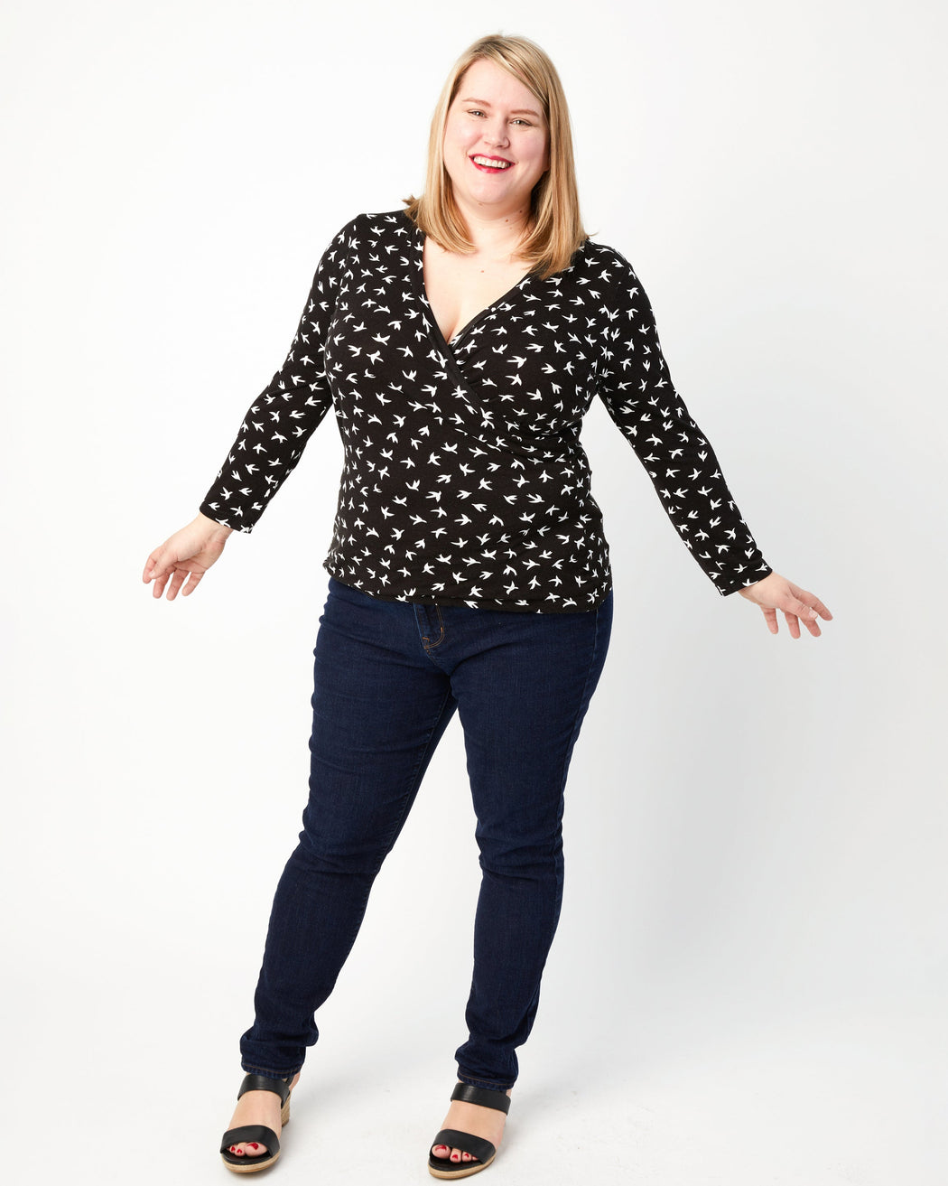 Woman wearing a black patterned top and dark jeans on a white background. This top is the Dartmouth Top sewing pattern from Cashmerette.