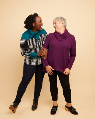 Two women standing together wearing colorful sweaters against a beige background. This sweater is the Tobin Sweater sewing pattern from Cashmerette.