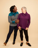 Two women standing together wearing colorful sweaters against a beige background. This sweater is the Tobin Sweater sewing pattern from Cashmerette.