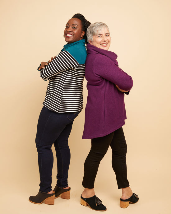 Two women standing back-to-back wearing colorful clothing against a beige background. This sweater is the Tobin Sweater sewing pattern from Cashmerette.