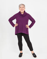 Woman wearing a purple cowl-neck sweater and black leggings on a white background. This sweater is the Tobin Sweater sewing pattern from Cashmerette.