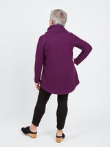 Person wearing a purple coat and black pants on a white background. This sweater is the Tobin Sweater sewing pattern from Cashmerette.