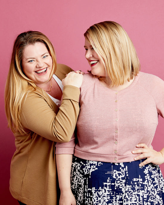 Two women posing together against a pink background. This cardigan is the Fuller Cardigan sewing pattern from Cashmerette.