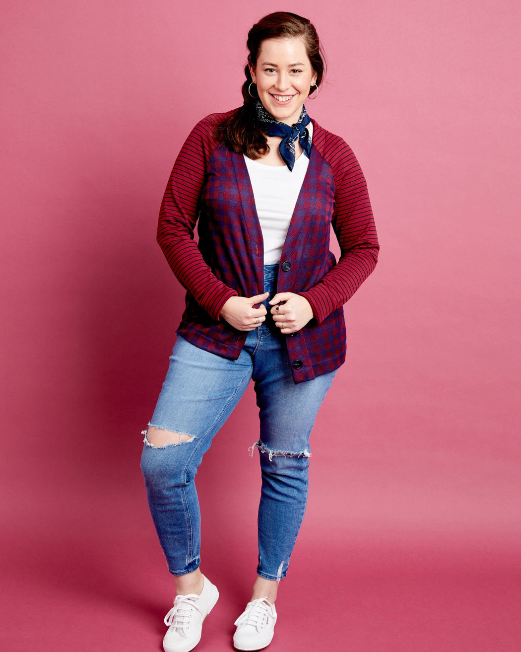 Woman wearing a red plaid shirt, white sneakers, and blue jeans on a pink background. This cardigan is the Fuller Cardigan sewing pattern from Cashmerette.