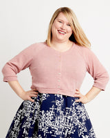 Woman wearing a pink cardigan and blue patterned skirt on a white background. This cardigan is the Fuller Cardigan sewing pattern from Cashmerette.