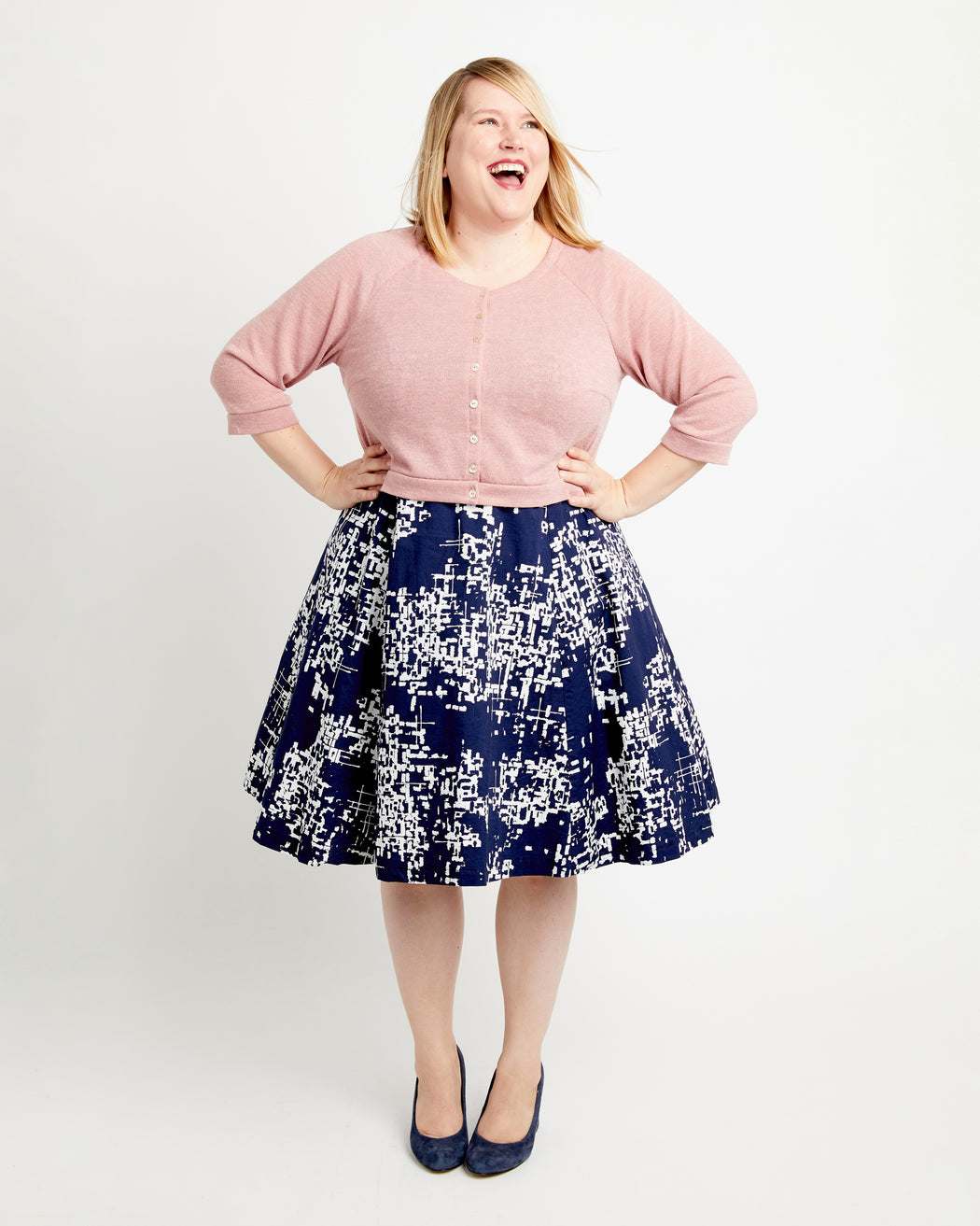 Woman wearing a pink sweater and navy patterned skirt on a white background. This cardigan is the Fuller Cardigan sewing pattern from Cashmerette.