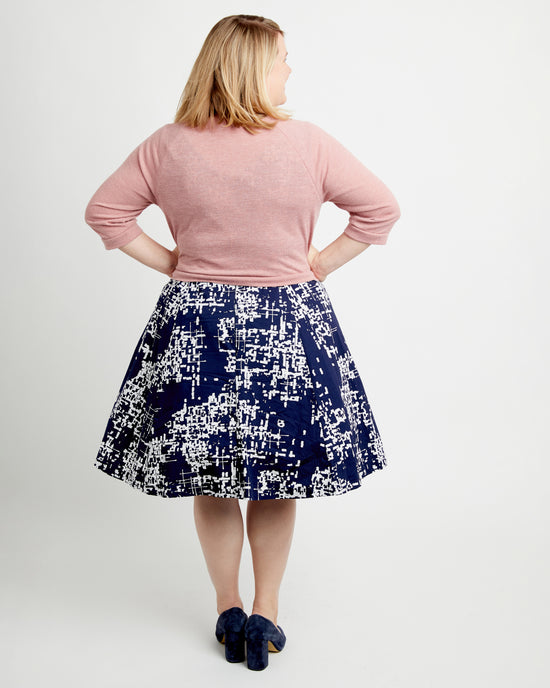 Woman wearing a pink sweater and navy skirt with white pattern on a plain background. This cardigan is the Fuller Cardigan sewing pattern from Cashmerette.