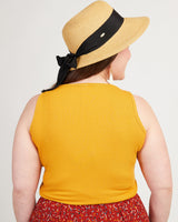 Person wearing a yellow sleeveless top and a straw hat with a black band on a plain background. This tank top is the Saybrook Tank sewing pattern from Cashmerette.