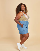 Woman wearing a striped tank top and blue shorts on a beige background. This tank top is the Saybrook Tank sewing pattern from Cashmerette.