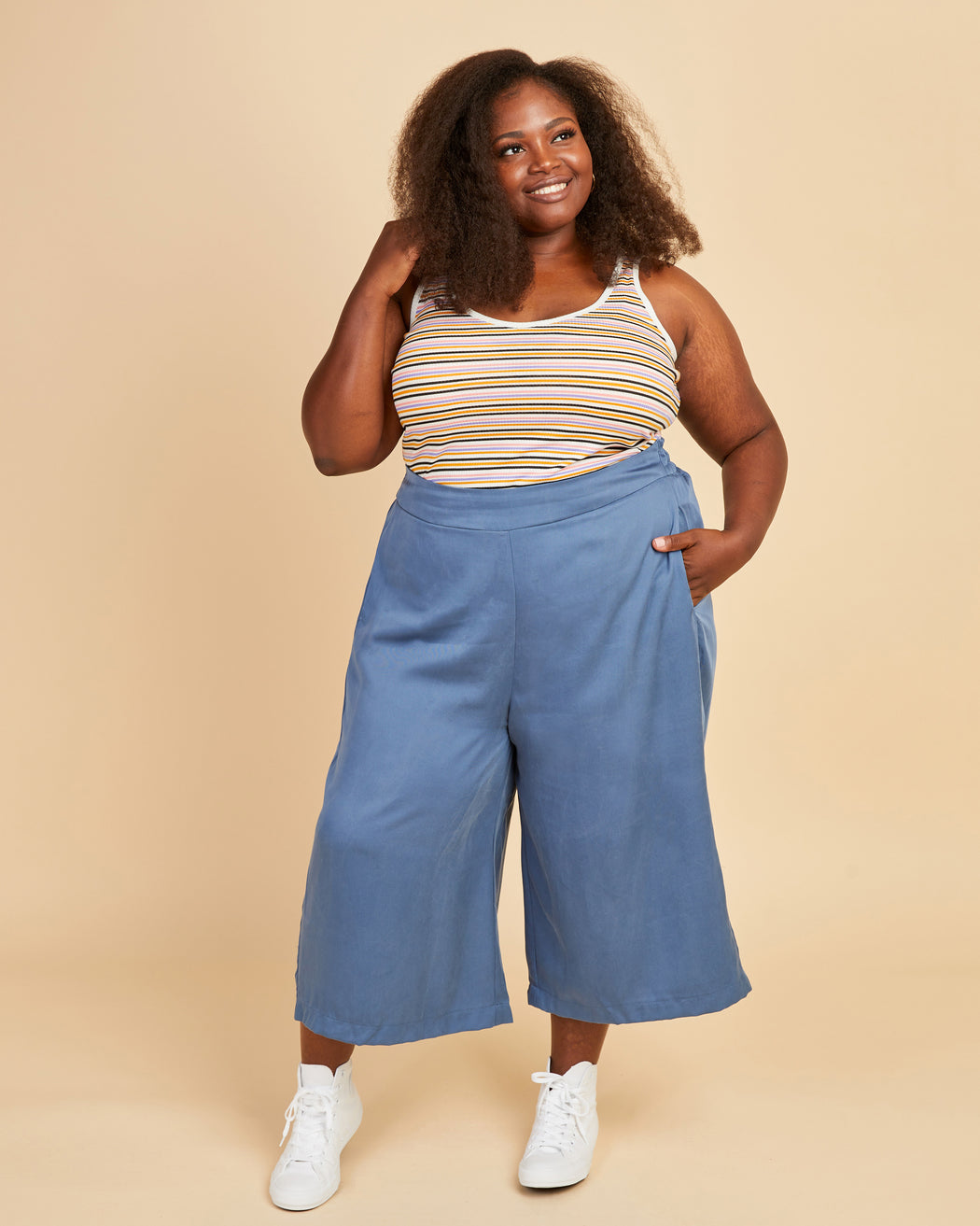 Woman wearing a striped tank top and blue wide-leg pants on a beige background. This tank top is the Saybrook Tank sewing pattern from Cashmerette.