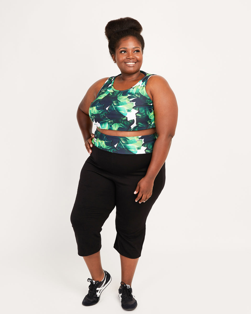 Woman wearing a green and black patterned sports bra and black capri leggings on a white background. This tank top is the Saybrook Tank sewing pattern from Cashmerette.