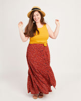 Woman wearing a yellow top and red floral skirt with a straw hat on a white background. This tank top is the Saybrook Tank sewing pattern from Cashmerette.