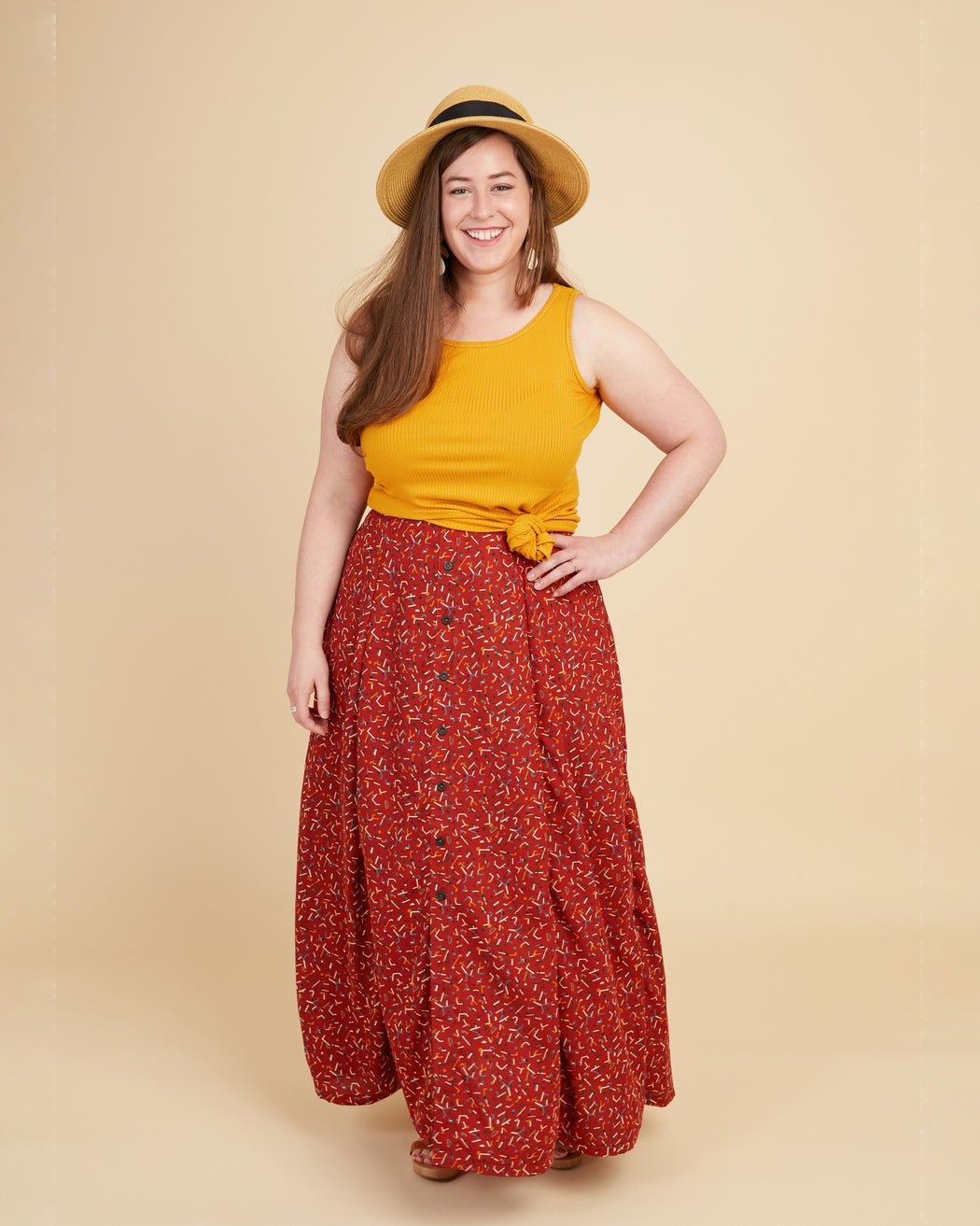 Woman wearing a yellow top and red floral skirt on a beige background. This tank top is the Saybrook Tank sewing pattern from Cashmerette.