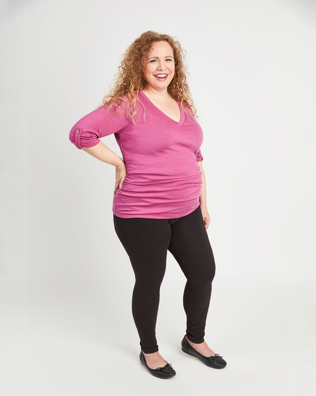 Woman wearing a pink top and black leggings on a white background. This t-shirt is the Brookline Maternity T-Shirt sewing pattern from Cashmerette.