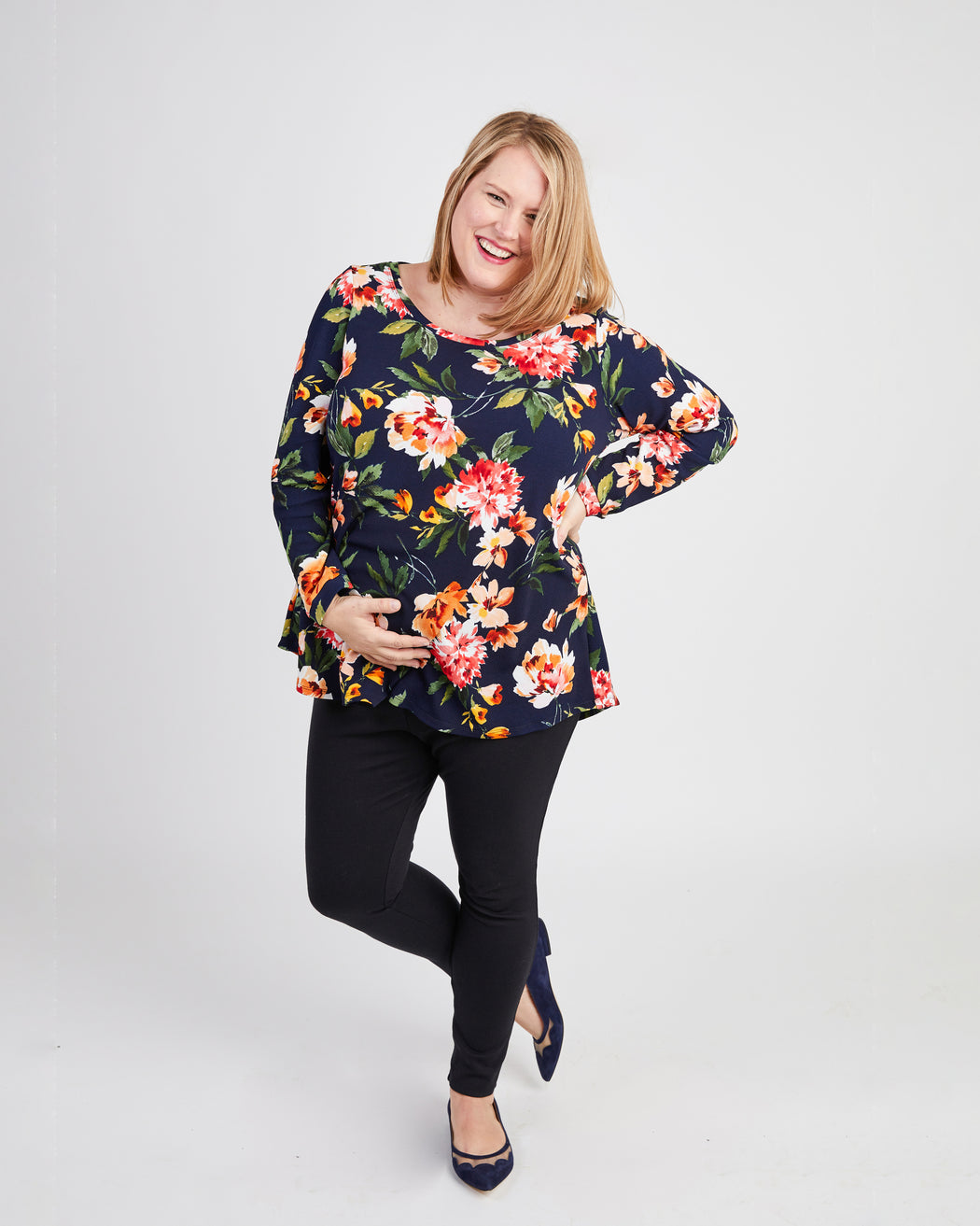 Woman wearing a floral top and black pants on a white background. This t-shirt is the Brookline Maternity T-Shirt sewing pattern from Cashmerette.