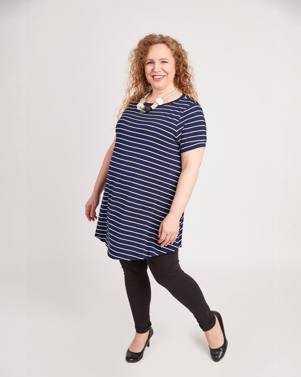 Woman wearing a navy striped dress on a white background. This t-shirt is the Brookline Maternity T-Shirt sewing pattern from Cashmerette.