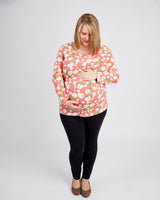 Woman wearing a pink floral top and black pants on a white background. This t-shirt is the Brookline Maternity T-Shirt sewing pattern from Cashmerette.