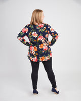 Woman wearing a floral blouse and black pants on a white background. This t-shirt is the Brookline Maternity T-Shirt sewing pattern from Cashmerette.