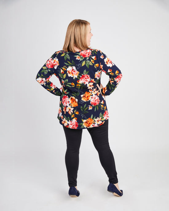 Woman wearing a floral blouse and black pants on a white background. This t-shirt is the Brookline Maternity T-Shirt sewing pattern from Cashmerette.
