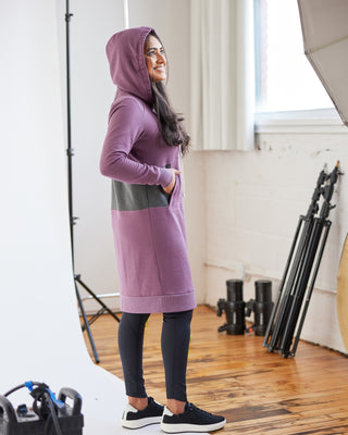 Person wearing a long purple hoodie in a studio setting with photography equipment. This hoodie is the Stanton Hoodie sewing pattern from Cashmerette.