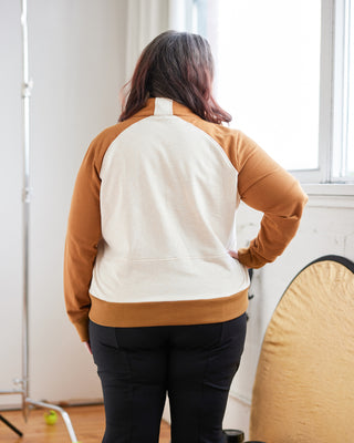 Person wearing a brown and white sweater in a room with a mirror and window. This hoodie is the Stanton Hoodie sewing pattern from Cashmerette.