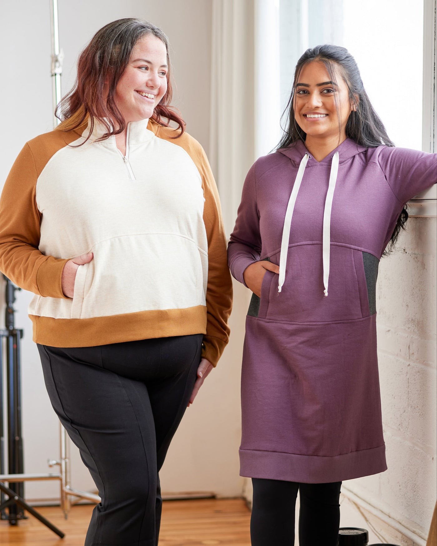 Two women wearing hoodies and black pants standing indoors. This hoodie is the Stanton Hoodie sewing pattern from Cashmerette.
