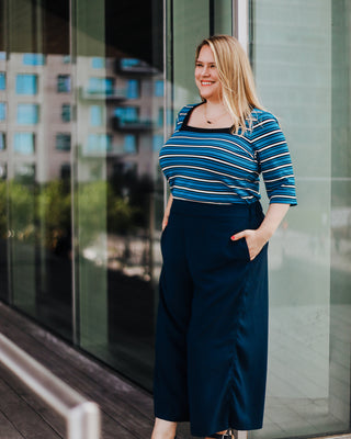Woman wearing a blue striped shirt and dark skirt standing in front of a glass building. This top is the Carlyle square neck t-shirt sewing pattern from Cashmerette.