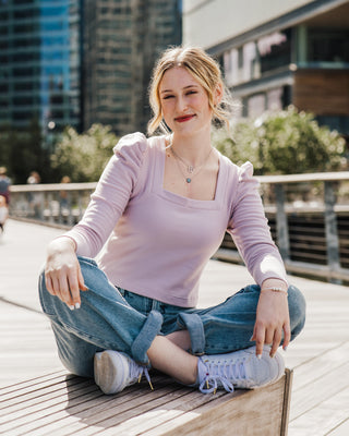 Woman sitting on a wooden bench outdoors with a cityscape background. This top is the Carlyle square neck t-shirt sewing pattern from Cashmerette.