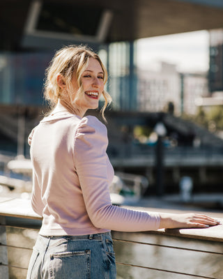 Woman in a pink sweater standing on a wooden deck with blurred background. This top is the Carlyle square neck t-shirt sewing pattern from Cashmerette.