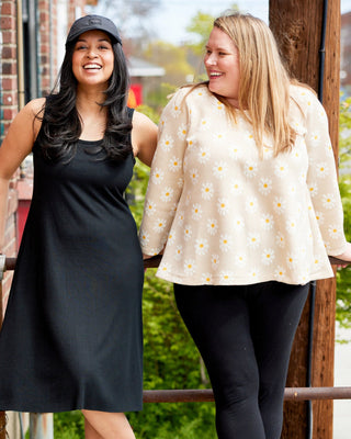 Two women standing outdoors, one in a black dress and white shoes, the other in a light-colored top and dark pants. This is the Wexford Top & Dress sewing pattern from Cashmerette.