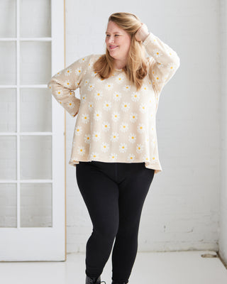 Woman wearing a cream floral blouse and black pants against a white background. This is the Wexford Top & Dress sewing pattern from Cashmerette.
