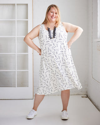 Woman wearing a white dress with black patterns in a minimal indoor setting. This is the Wexford Top & Dress sewing pattern from Cashmerette.