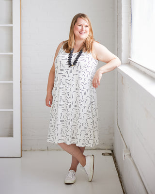 Woman wearing a white dress with black patterns in a bright room. This is the Wexford Top & Dress sewing pattern from Cashmerette.