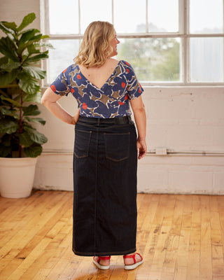 Woman wearing a patterned top and black skirt standing in a room with wooden floor and large windows. This top is the Kenwin Raglan T-Shirt sewing pattern from Cashmerette.