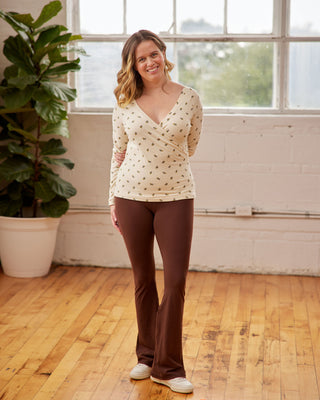 Woman wearing a white long-sleeve top with a pattern and brown pants standing in a room with wooden floors and large windows. This top is the Kenwin Raglan T-Shirt sewing pattern from Cashmerette.
