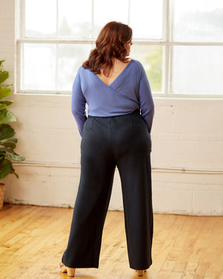 Woman wearing a blue top and black pants standing in a room with large windows. This top is the Kenwin Raglan T-Shirt sewing pattern from Cashmerette.
