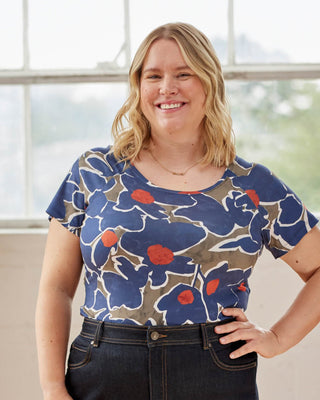 Woman wearing a blue floral top with red flowers, standing indoors. This top is the Kenwin Raglan T-Shirt sewing pattern from Cashmerette.