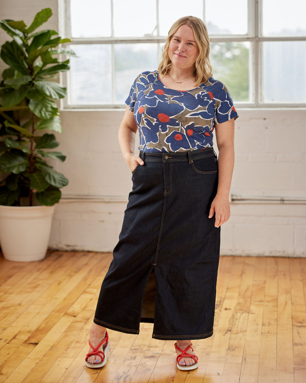 Woman wearing a blue floral top and dark jeans standing in a room with wooden floor and large windows. This top is the Kenwin Raglan T-Shirt sewing pattern from Cashmerette.