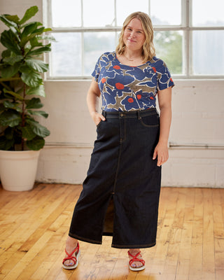 Woman wearing a blue floral top and dark jeans standing in a room with wooden floor and large windows. This top is the Kenwin Raglan T-Shirt sewing pattern from Cashmerette.