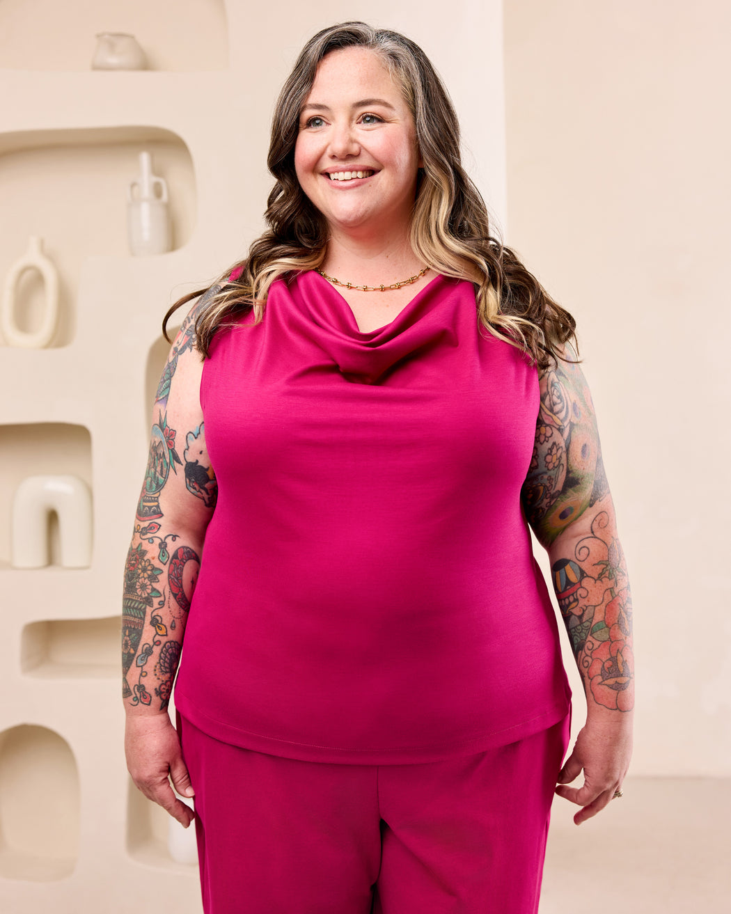 Woman posing with a pink cowl neck top and matching pink pants in front of a cream colored background.  This is the Amesbury Cowl Top sewing pattern from Cashmerette.