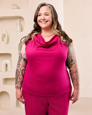 Woman posing with a pink cowl neck top and matching pink pants in front of a cream colored background.  This is the Amesbury Cowl Top sewing pattern from Cashmerette.