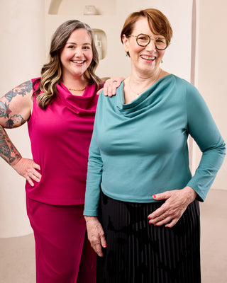 Two women posing together in front of a cream colored background. This is the Amesbury Cowl Top sewing pattern from Cashmerette.