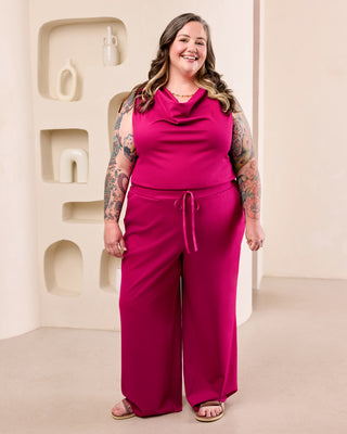 Woman posing with a pink cowl neck top and matching pink pants in front of a cream colored background.  This is the Amesbury Cowl Top sewing pattern from Cashmerette.