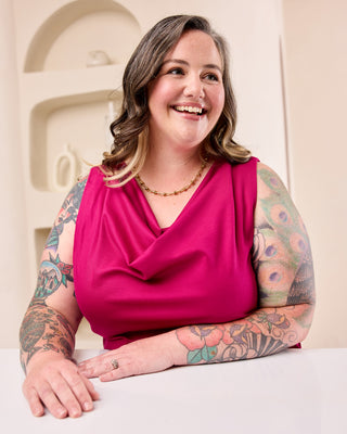 Woman posing with a pink cowl neck top in front of a cream colored background.  This is the Amesbury Cowl Top sewing pattern from Cashmerette.