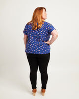 Woman wearing a blue polka dot shirt and black pants on a white background. This top is the Cedar Dolman Top sewing pattern from Cashmerette.