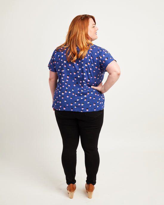 Woman wearing a blue polka dot shirt and black pants on a white background. This top is the Cedar Dolman Top sewing pattern from Cashmerette.