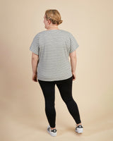 Person wearing a striped t-shirt and black leggings on a beige background. This top is the Cedar Dolman Top sewing pattern from Cashmerette.