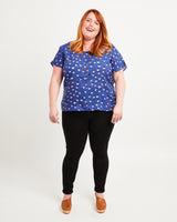 Woman wearing a blue polka dot shirt and black pants on a white background. This top is the Cedar Dolman Top sewing pattern from Cashmerette.