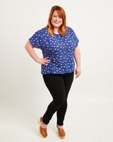 Woman wearing a blue polka dot top and black leggings on a white background. This top is the Cedar Dolman Top sewing pattern from Cashmerette.