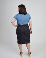 Woman wearing a blue t-shirt and dark denim skirt on a plain background. This skirt is the Ellis Denim Skirt sewing pattern from Cashmerette.